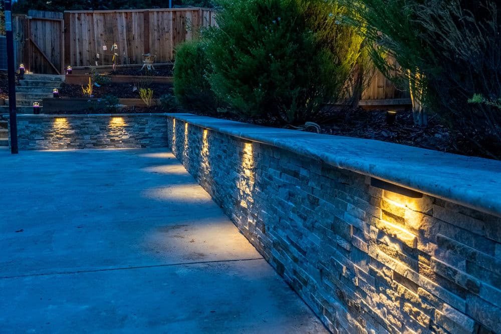 Illuminated stone wall in a landscaped backyard at night with soft lighting accent.