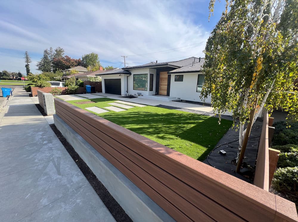 Modern home exterior with landscaped lawn, stone pathway, and wooden fence. Sunny day.
